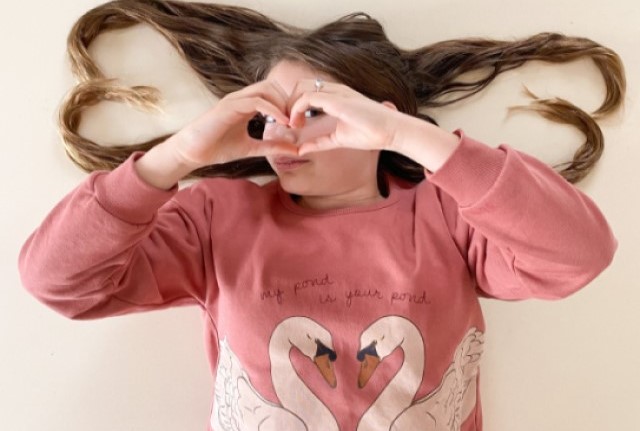 Brustbild person, rosa Pullover, Schwanenmotiv, Aufschrift "my pond is your pond", lange Haare, handgeformtes Herz.