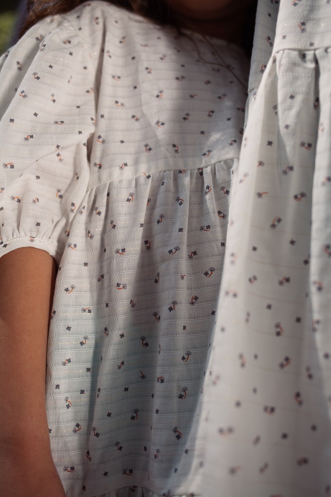 4-2 Kinderkleid, weiß, kurzes ärmel, dezenter Musteraufdruck mit kleinen Figuren und Punkten.