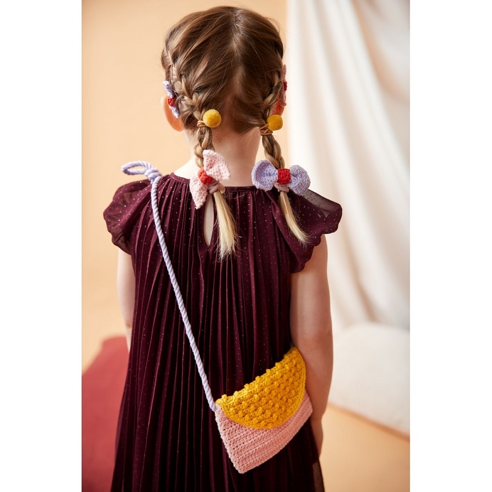 9511185-Haargummi-Schleife-sortiert-2 Kind mit geflochtenem Haar, Haarschmuck, dunkelrotes Kleid, gehäkelte Tasche mit gelbem und rosa Muster, Schulterriemen.