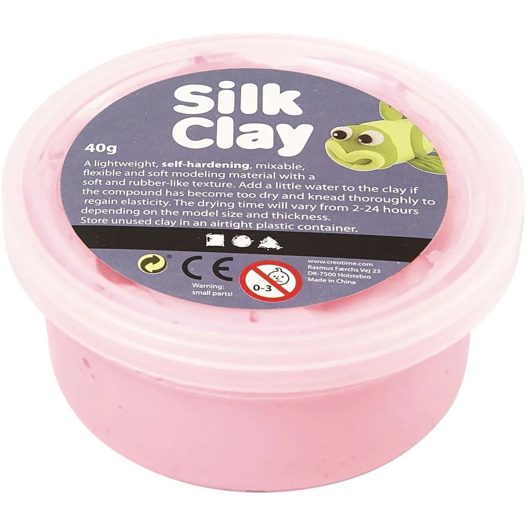 Rosa Modelliermasse im Kunststoffbehälter, Aufdruck "Silk Clay", grüne Cartoon-Figur, Aufschrift "40g", Warnsymbol 0-3 Jahre, CE-Kennzeichnung.