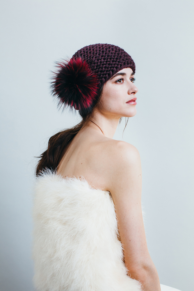 88KA1_lookbook_hires_2587112ebbdbee Strickmütze dunkelrot, großer flauschiger Bommel in Rot-Schwarz, getragen von Frau, seitliches Profil, schlichtes Design.