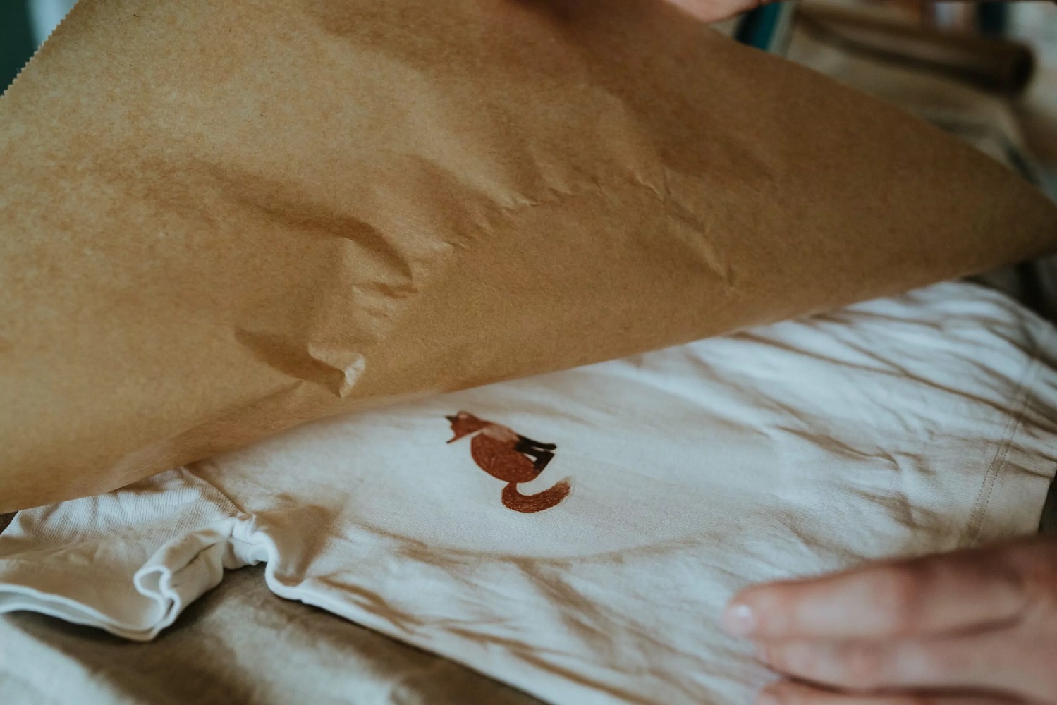 2022-02-nuuk-138-scaled T-Shirt, weiß, Fuchsaufdruck, braun, Verpackung aus Packpapier, teilweise sichtbar.