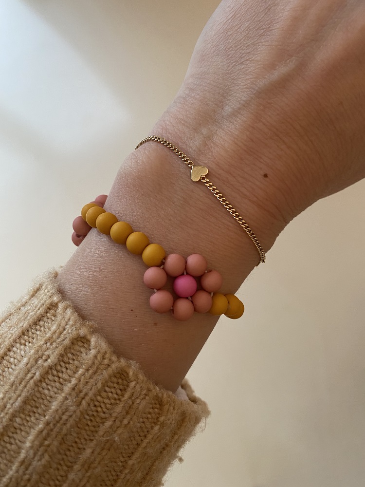 IMG_4974 Goldfarbenes Armband mit Herzanhänger, Perlenarmband in Gelb und Rosa, Blumenmuster; Arm in beige gestricktem Pullover.