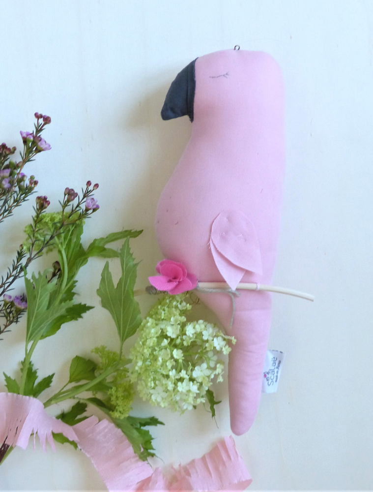 Scala-Ernesto-le-perroquet Stofftier, Papagei, rosa, schwarzer Schnabel, geschlossene Augen, rosa Stoffblume, Label am Schwanz.