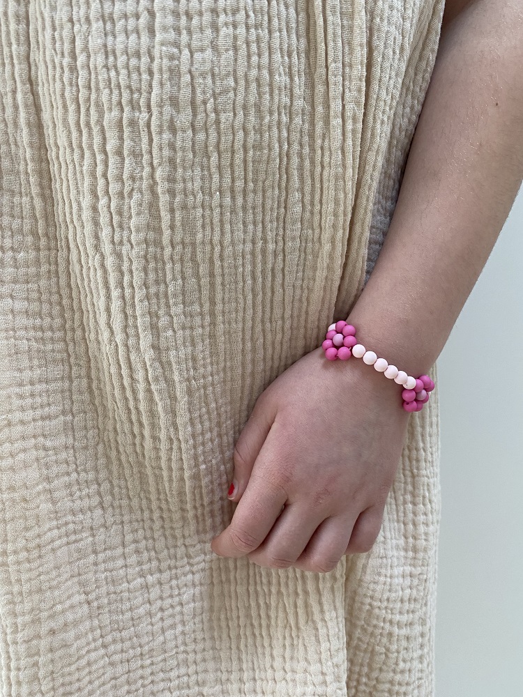 IMG_4899 Beiges, grob strukturiertes Kleid; Kind; Armreif mit pinken und weißen Perlen; Dekor in Blumenform; Hand mit rotem Nagellack.