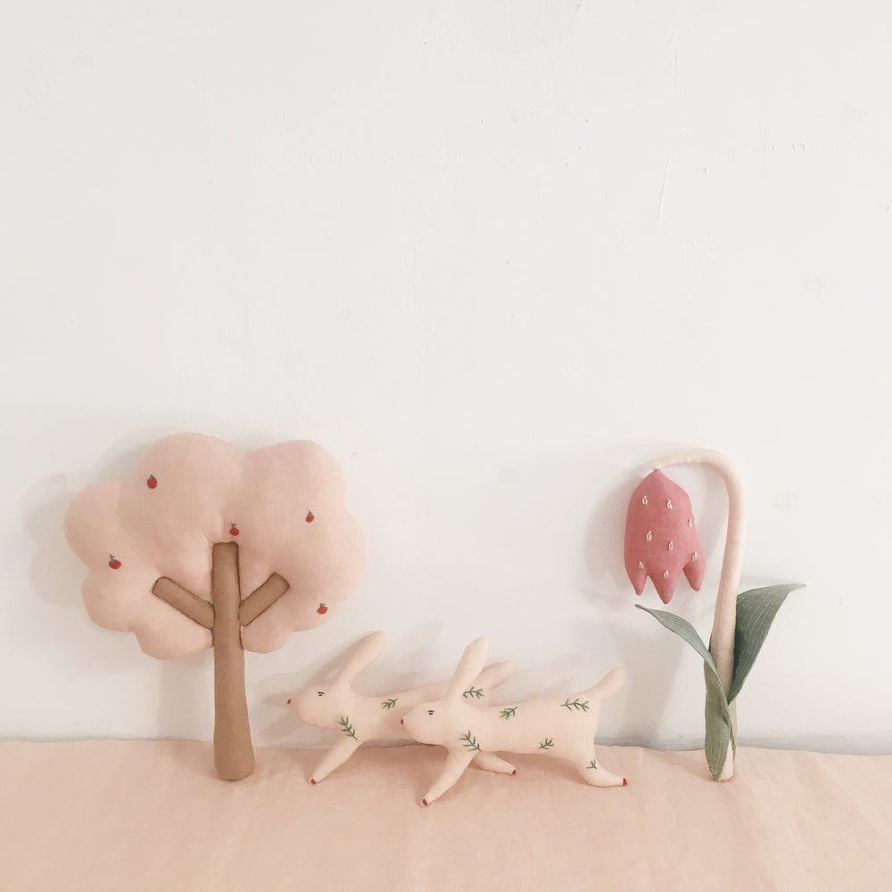 6BFA71B0-531D-4351-B225-8B90671B6FE3 Stofftiere, sanfte Farben; rosa Baum mit Äpfeln; zwei beige Hasen mit Blattmotiven; rosa Blume mit grünem Blatt.