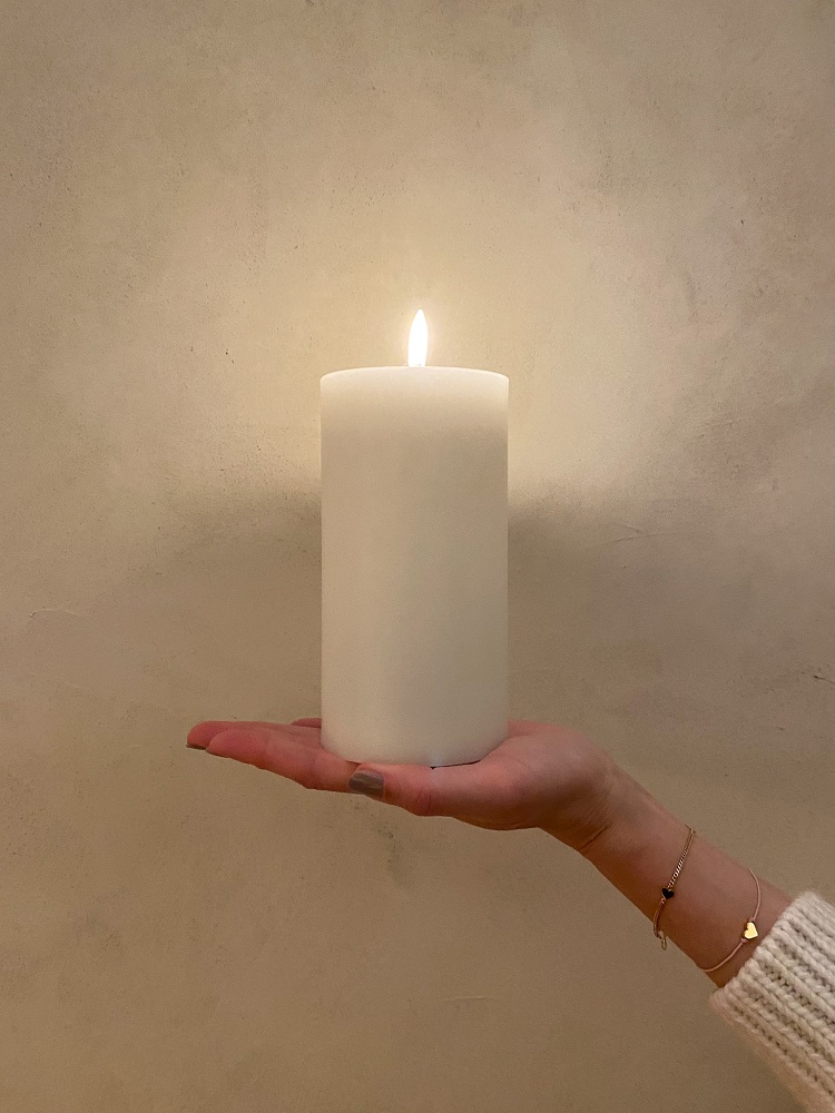 Weiße Stumpenkerze, brennend, gehalten auf Hand, dezenter Hintergrund.