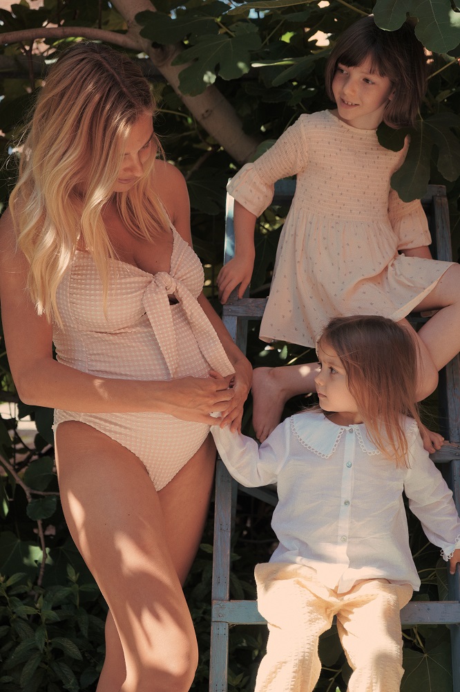 KS2919-FRESIA-MAMA-PREGGI-SWIMSUIT-ROSE-SMOKE-Extra-1 Badeanzug, rosa, Schleife vorne; Kinderkleidung: Mädchenkleid, beige, gepunktet, langärmelig; Kind: weiße Bluse, gelbe Hose; Leiter, Holz.
