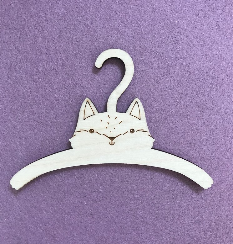 IMG_2792 Kleiderbügel, Holz, helles Material, Katzenmotiv, eingravierte Details, lila Hintergrund.