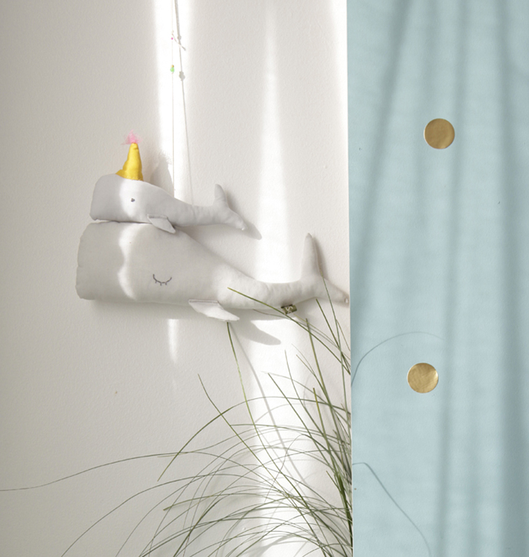 Scala-Calypso-gris-1 Stoff-Wal, weiß, kleiner Wal auf großem Wal, gelber Partyhut, Aufhänger, Wanddeko, links von blauem Vorhang mit goldenen Punkten.