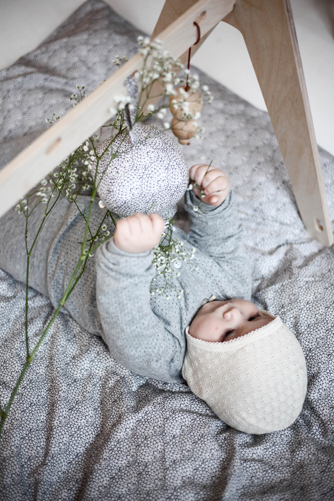 10007-MARSHMALLOW-BEDDING-1 Babyspielmatte grau, strukturierter Stoff; Babyspielzeug aus Holz und Stoff, naturfarben; Baby Strampler grau, Mütze creme; Baby Holzspielbogen.