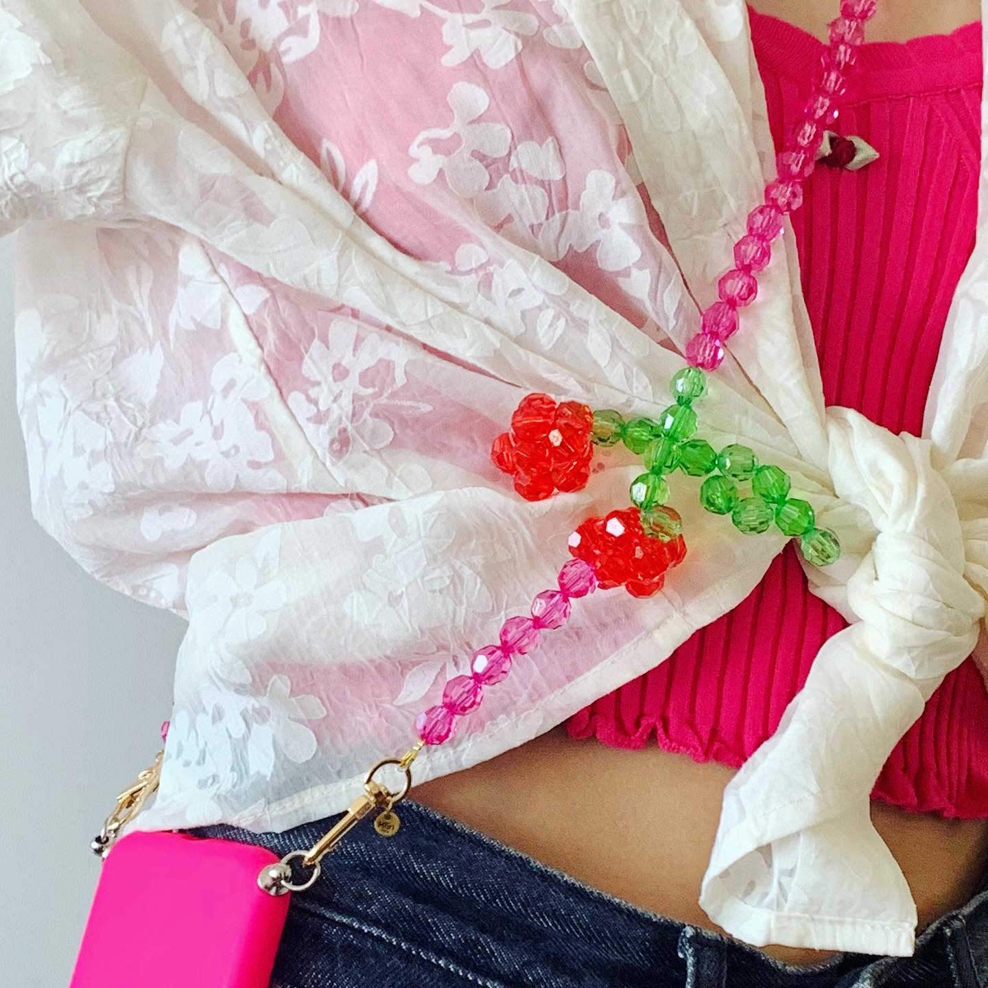 Handykette, bunte Perlen, Kirschdesign, rosa und grün, goldene Karabiner, weißes Blumenmuster, rotes Top, blaue Jeans.