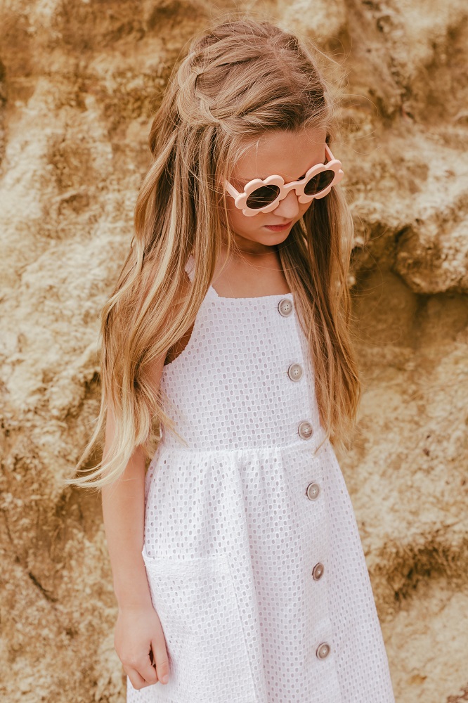 39ORANGEFIZZ_3 Weißes Kinderkleid, ärmellos, Knopfleiste, Seitentasche, rosa Sonnenbrille mit Blumenform.