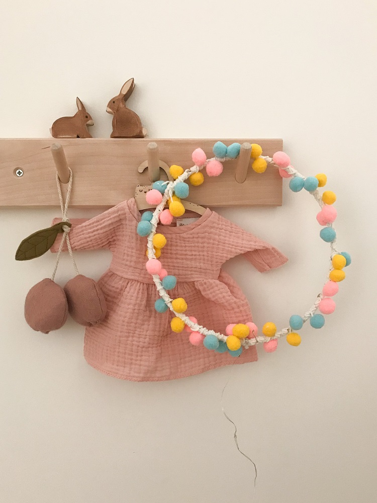 IMG_4948 Rosa Kinderkleid, grobe Struktur, Pompon-Girlande in Rosa, Gelb, Blau, hölzerne Kleiderhaken, Holzhasen auf Leiste, gepolsterte Anhänger.
