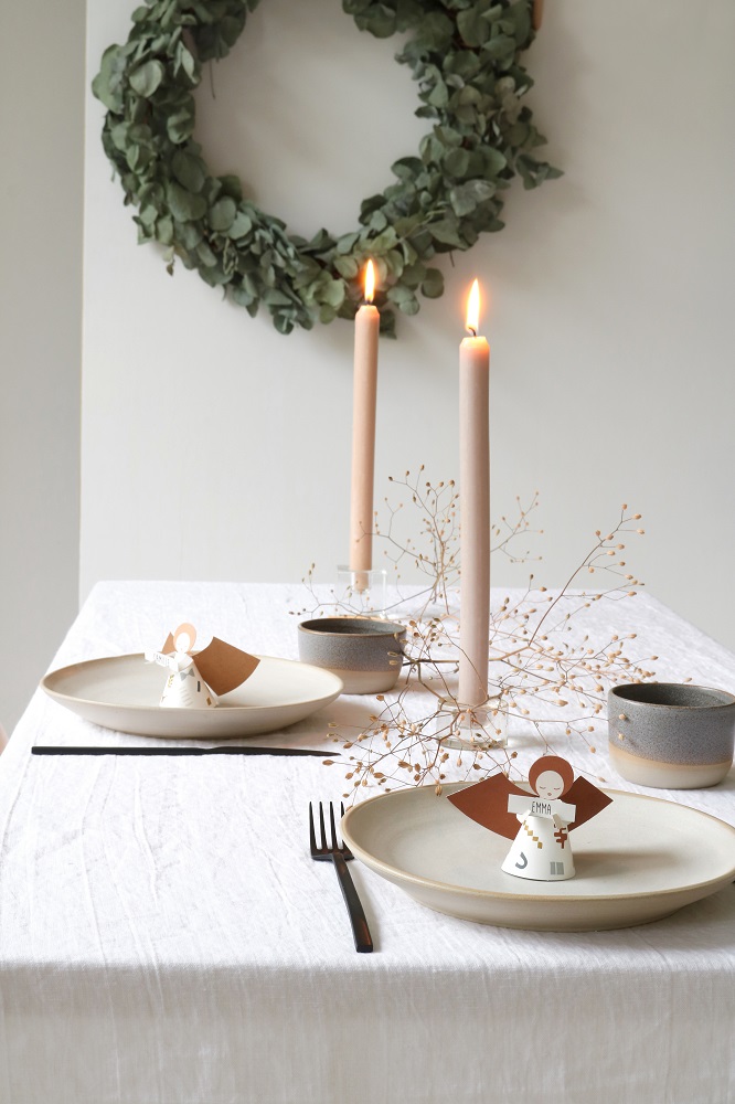 fridur-new-25 Tischgedeck, beiger Teller, schwarze Gabel, hellbraune Tassen, beige Kerzen, weißes Tischtuch, Engel-Namenskarten, Trockenblumen, Kranz.