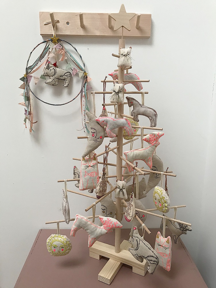 F8574D51-460F-4C69-B797-302E5E3B617D-002 Holzbaum mit handgefertigten Stoffanhängern; Tiere und Muster; Beige, Rosa, Grau; dekorativer Stoffkranz mit Bändern und Glocke; minimalistisch; Fertigung aus naturbelassenem Holz; schlichtes Design.