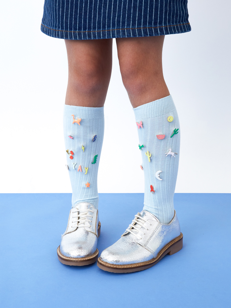 Everyday17-Access-843-E1 Kinderkniestrümpfe, hellblaue Farbe, bunte Aufnäher mit Tier- und Pflanzenmotiven, silberne Schnürschuhe, blau-weißer Nadelstreifenrock.