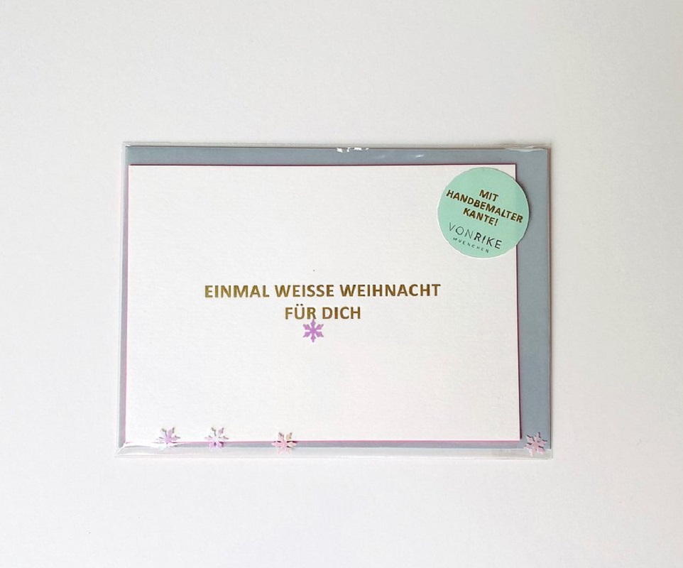 7a75ef_a7bafb04617647278aa352aa4ae7f8e4_mv2 Weihnachtskarte, weiß mit goldener Aufschrift "Einmal weiße Weihnacht für dich", lila Schneeflocken, runder grüner Aufkleber "Mit handbemalter Kante", verpackt.