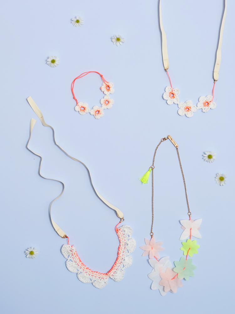 Everyday17-Access-476-E1 Ketten und Armband mit Blumenmotiven, weiß, rosa und neon-orange; Halsketten mit Stoffblumen und eine mit Quastenanhänger; Hintergrund hellblau.