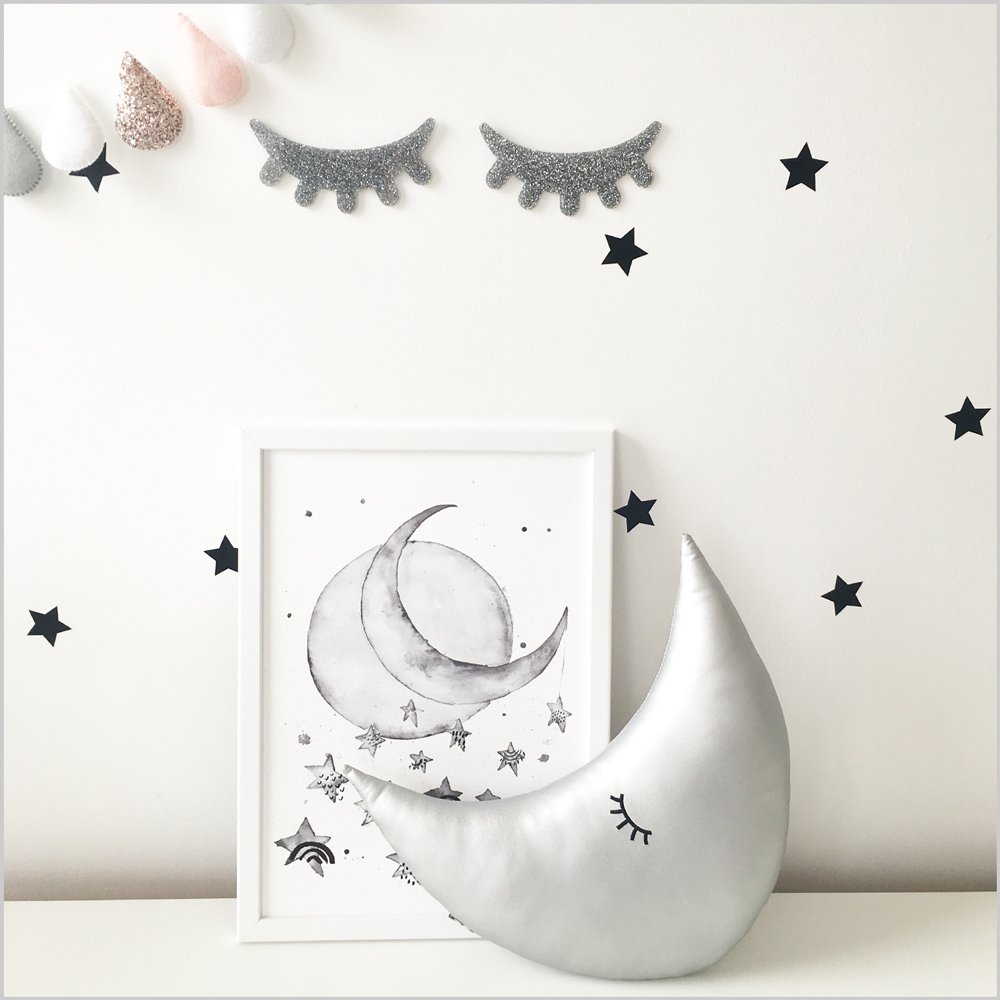 DEsilver2 Mondförmiges Kissen silber, schwarzer Wimpernaufdruck, Sterne an der Wand, Wandbild mit Mondmotiv, schlichte Farbpalette, Wolkengirlande rosa und grau, glitzernde Wimpern-Deko, minimalistische Gestaltung.