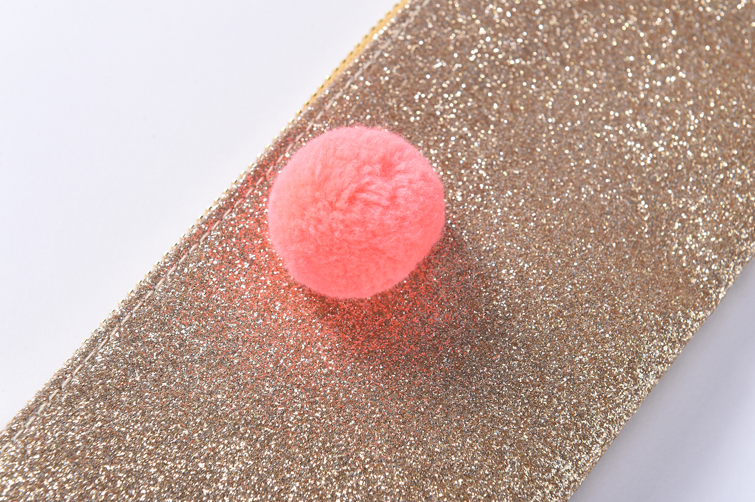 OUSTINA_6 Glitzernde goldene Oberfläche, darauf ein rosa flauschiger Pompon.
