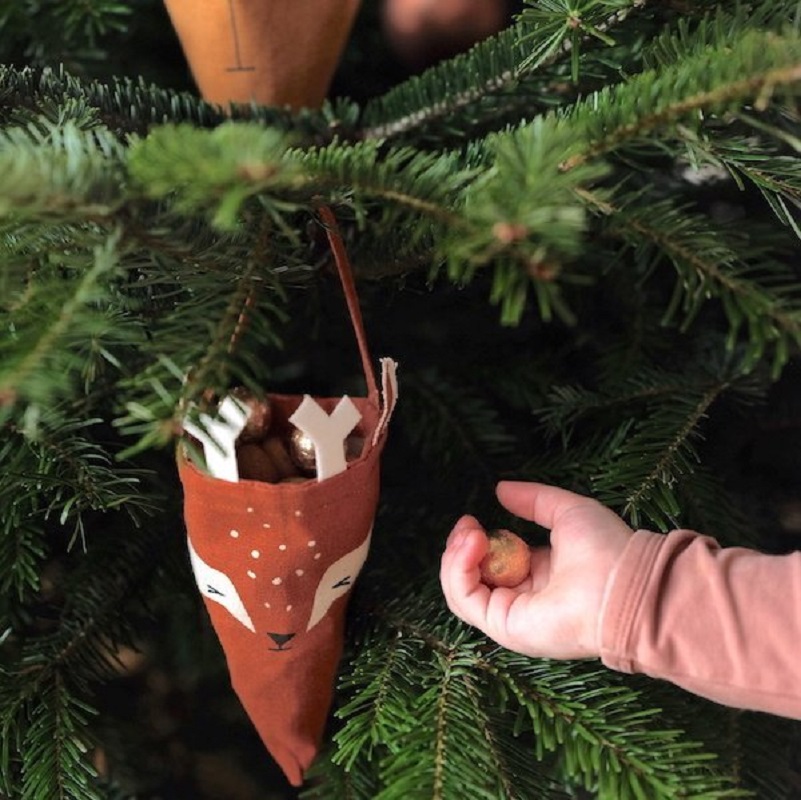 FBL20christmas20cones201 Brauner Stoffbeutel mit Rentiergesicht, gefüllt mit Nüssen, Tannenzweig, Kinderhand mit Haselnuss.