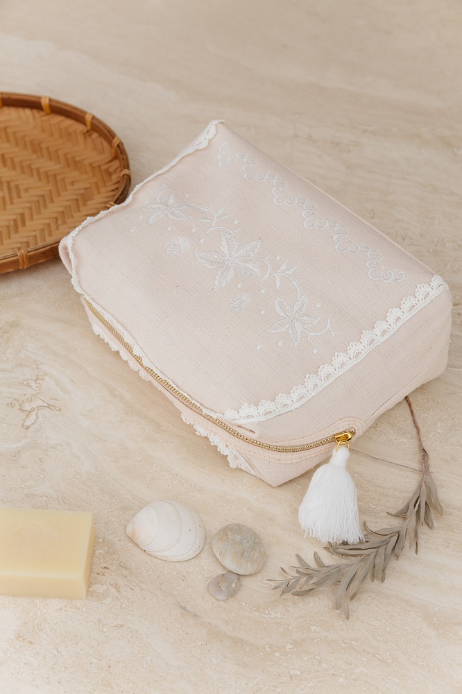 home-large-pocket-teiki-blush-1 Kosmetiktasche beige, Stickmuster weiß, Reißverschluss mit weißem Quastenanhänger, Spitze am Rand, rechteckige Form.