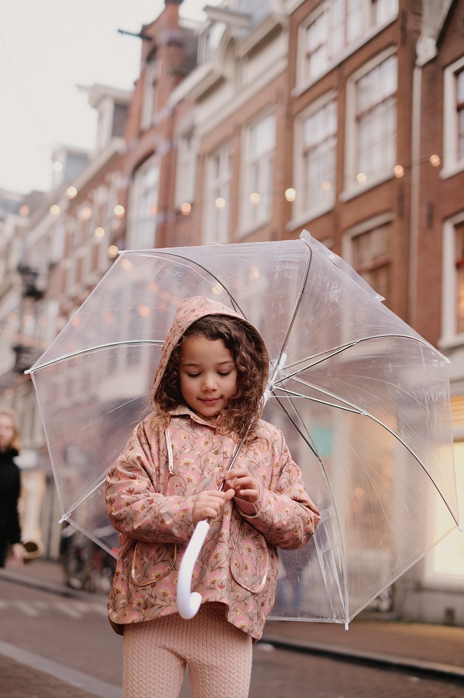 Kinderregenjacke, rosa mit Blumenmuster; transparenter Regenschirm mit weißem Griff.