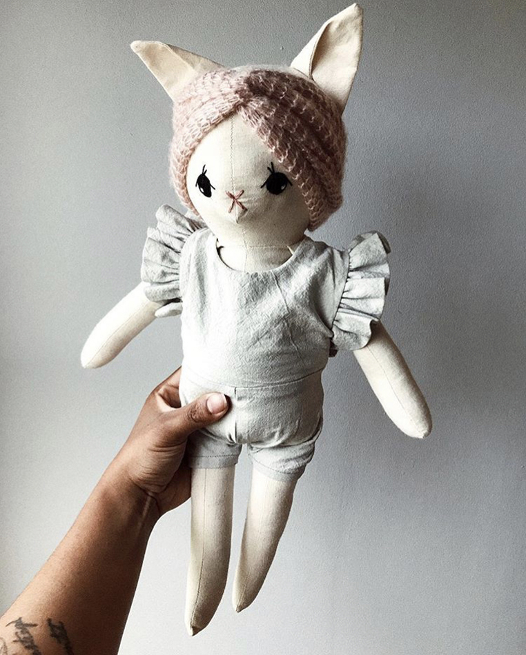 IMG_4545 Stofftier Katze, cremeweiß, gestricktes rosa Stirnband, graues Kleid mit Rüschenärmeln.