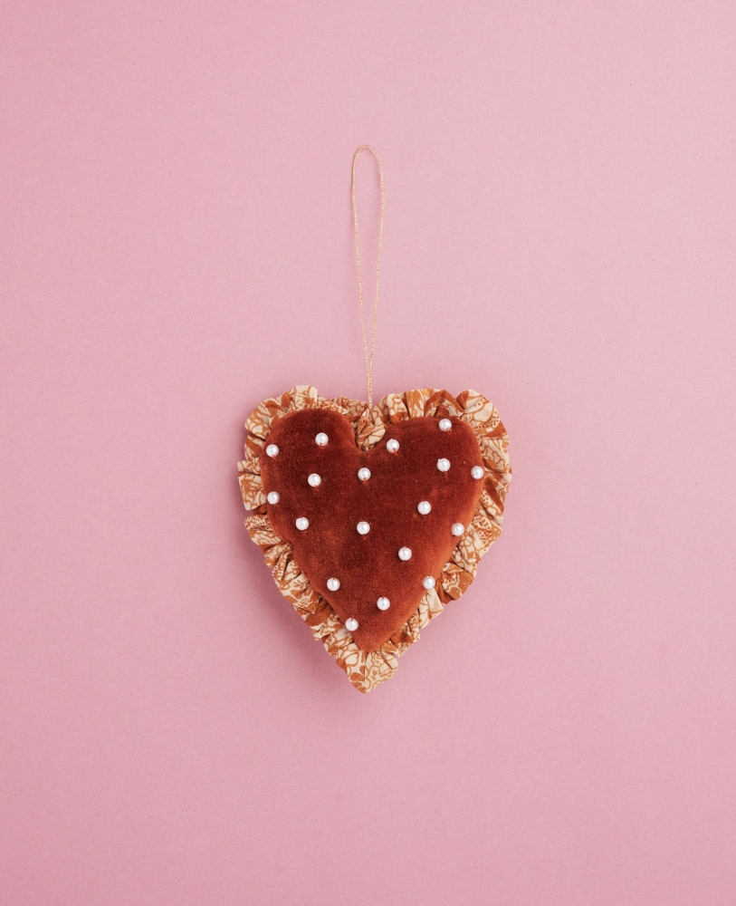 Velvet-Heart-Ornament-Cheesecake Herzförmiger Anhänger, braun, Plüschoptik, dekorative weiße Perlen, goldener Aufhänger, rosa Hintergrund.