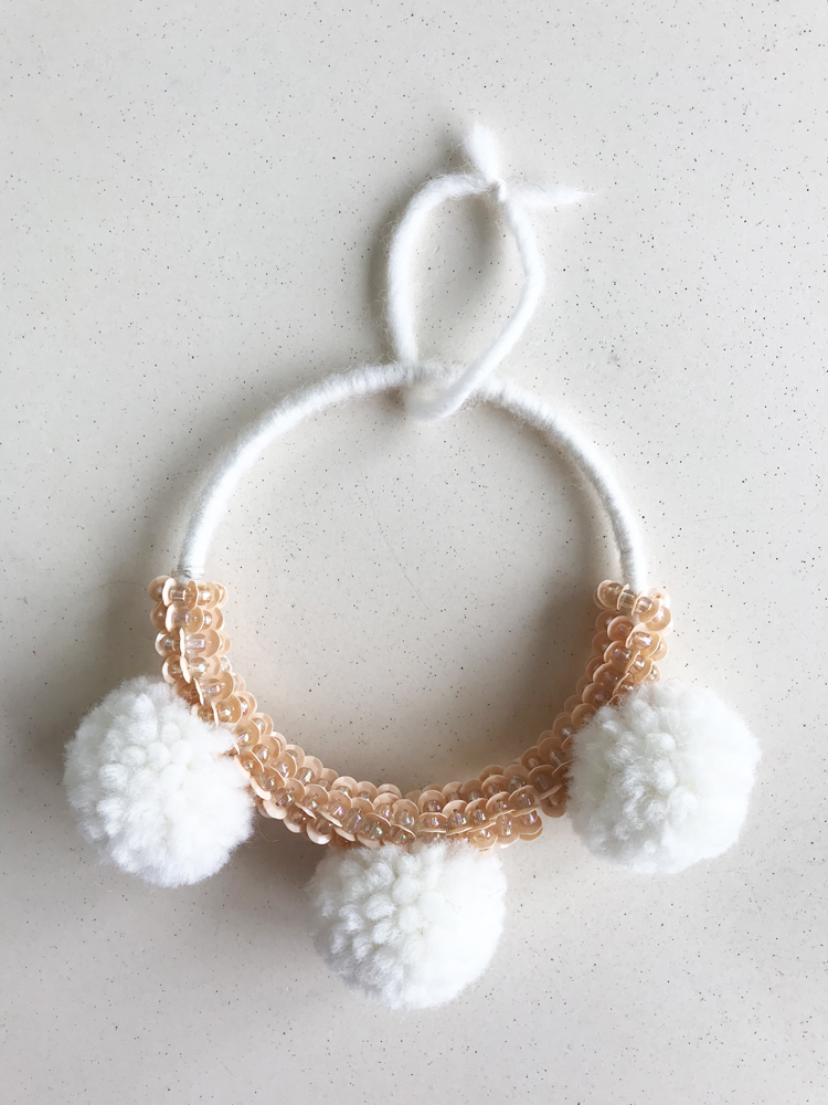 IMG_2880 Weiße Handykette mit drei großen weißen Pompons, transparenten Perlen in Pfirsichton, elastisches Material, texturierte Oberfläche.