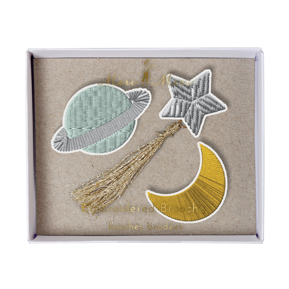 50-0113 Stickabzeichen-Set, hellgrüner Planet mit Ring, silberner Stern mit goldenem Schweif, gelber Mond, auf braunem Karton.