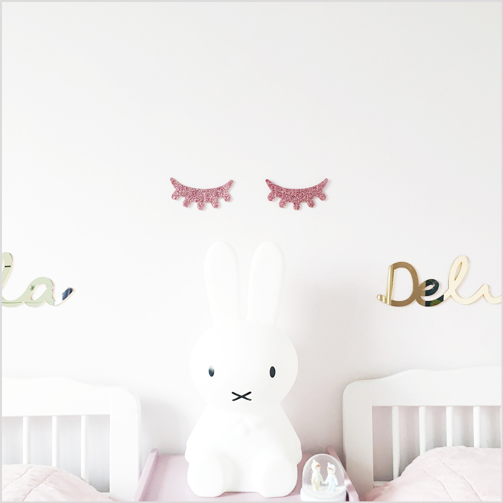 pink3 Weiße Hasenlampe, rosa Glitzer-Wimpernaufkleber an der Wand, Schriftzug "Dela" in goldener glänzender Optik, zwei Betten mit weißen Rahmen.