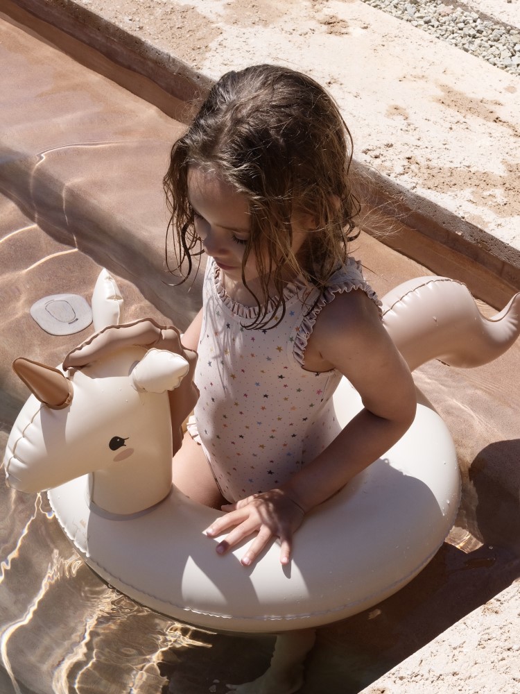 KS4726-TWINKLE-SWIMSUIT-STAR-MULTI-Extra-2 Aufblasbarer Schwimmring, Einhorn-Design, cremefarben, mit Ohren und Horn, Kinderspielzeug, Pool-Zubehör. Mädchen trägt Badeanzug mit Sternen-Muster.