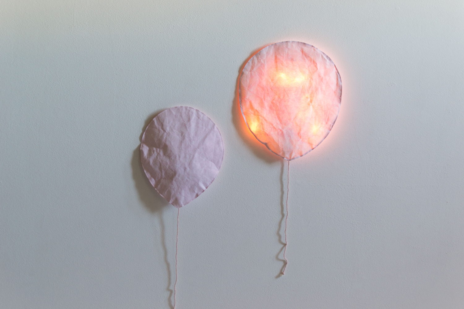 lightpink2 Papierlampen in Luftballonform, zwei Größen, zartrosa, Wandmontage, eine Lampe leuchtet mit warmem Licht, angedeutete Schnüre.