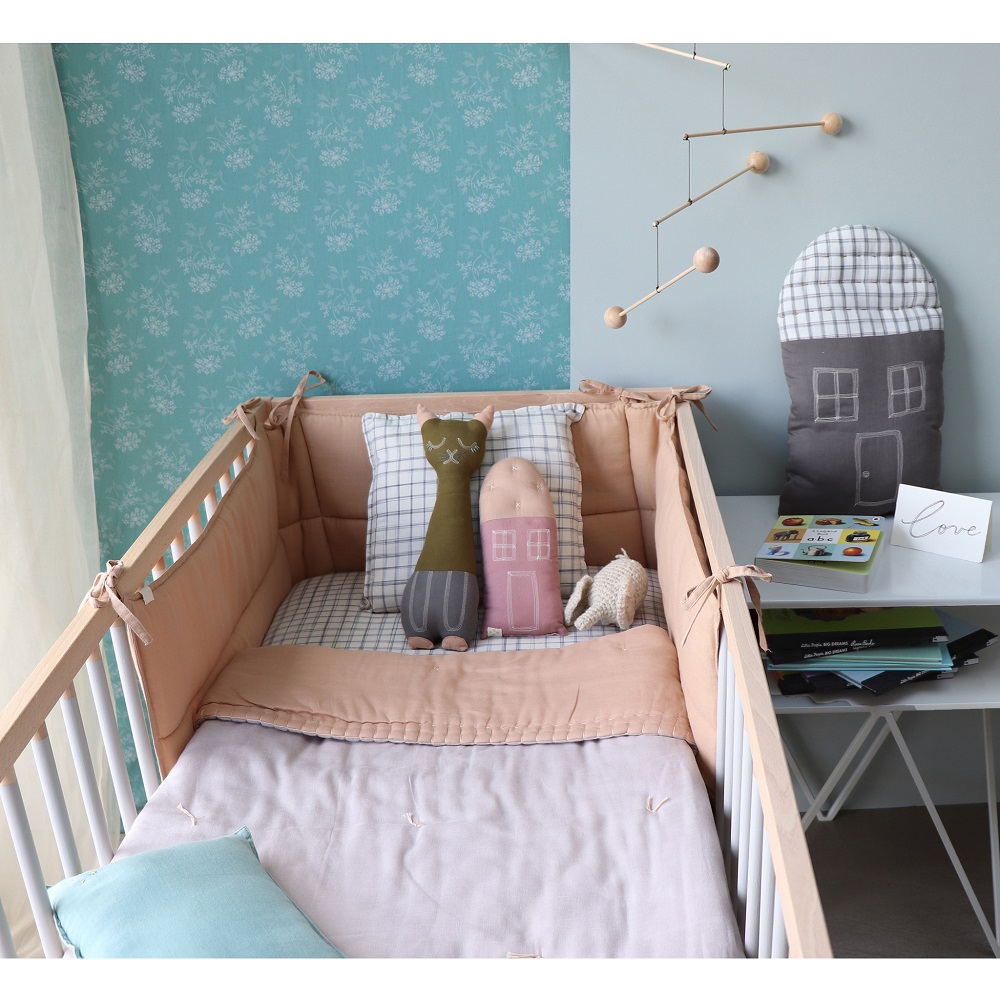 peach_blossom_bumper Babybett, Holz, beige Nestchen; Kissen im Haus- und Katzendesign, grün und rosa; karierte Kissen, Stoffhase; graues Hauskissen an der Wand; blau-graue Bettwäsche.