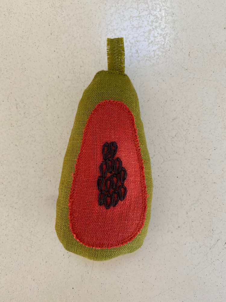 IMG_0428 Stoffspielzeug in Form einer Papaya, grüne Außenseite, rote Innenseite mit schwarzen Samenstickereien, kleine Schlaufe oben.