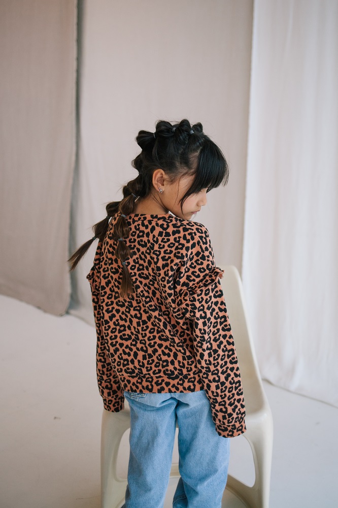 3-20 Kinderpullover, Leopardenmuster, orange-schwarz, Rüschen an den Schultern, kombiniert mit blauer Jeans.