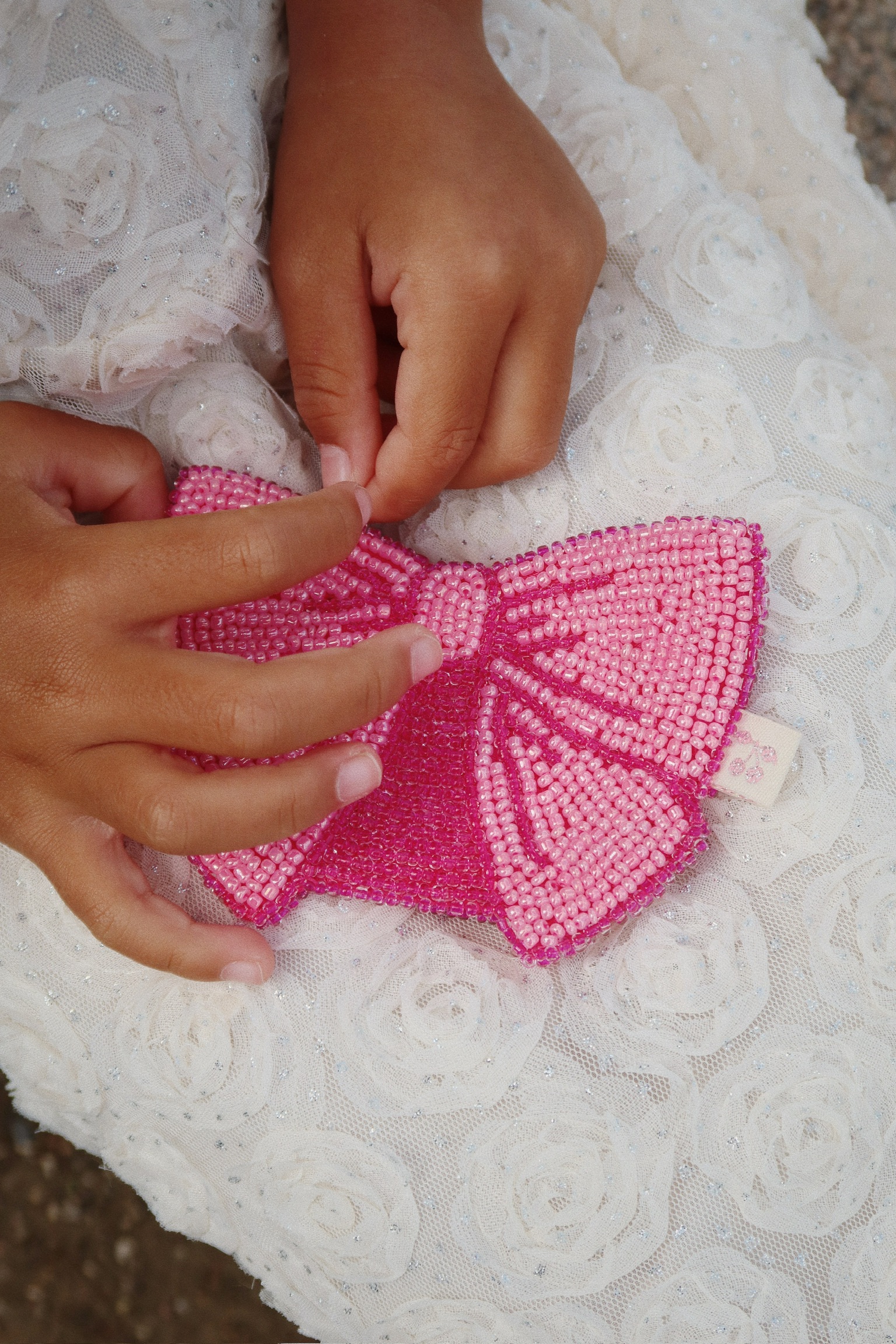 Handtasche, pink, perlenbesetzt, Schleifendesign, Detailaufnahme, weiße Stoffunterlage mit Rosenmuster.