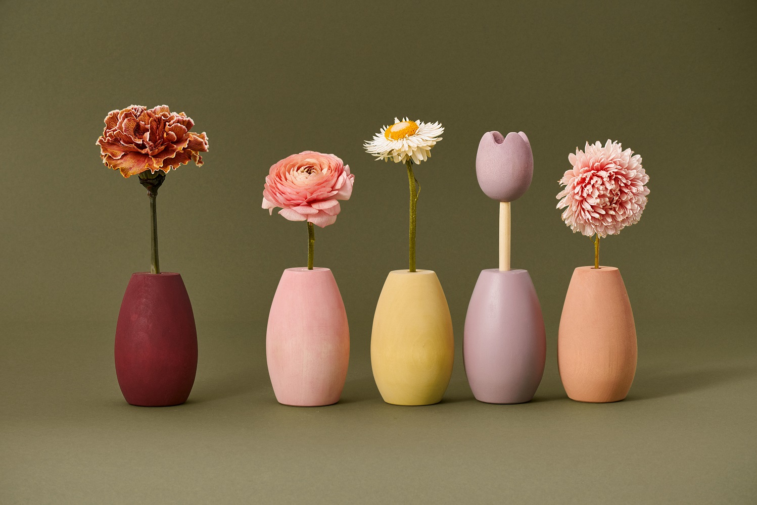 200904_Raduga_Grez_campaign5316 Fünf bunte Keramikvasen in Rot, Rosa, Gelb, Lila und Orange, jede mit einer dekorativen Blume: Nelke, Ranunkel, Margerite, Tulpe, Chrysantheme. Schlichtes, modernes Design auf einfarbigem Hintergrund.