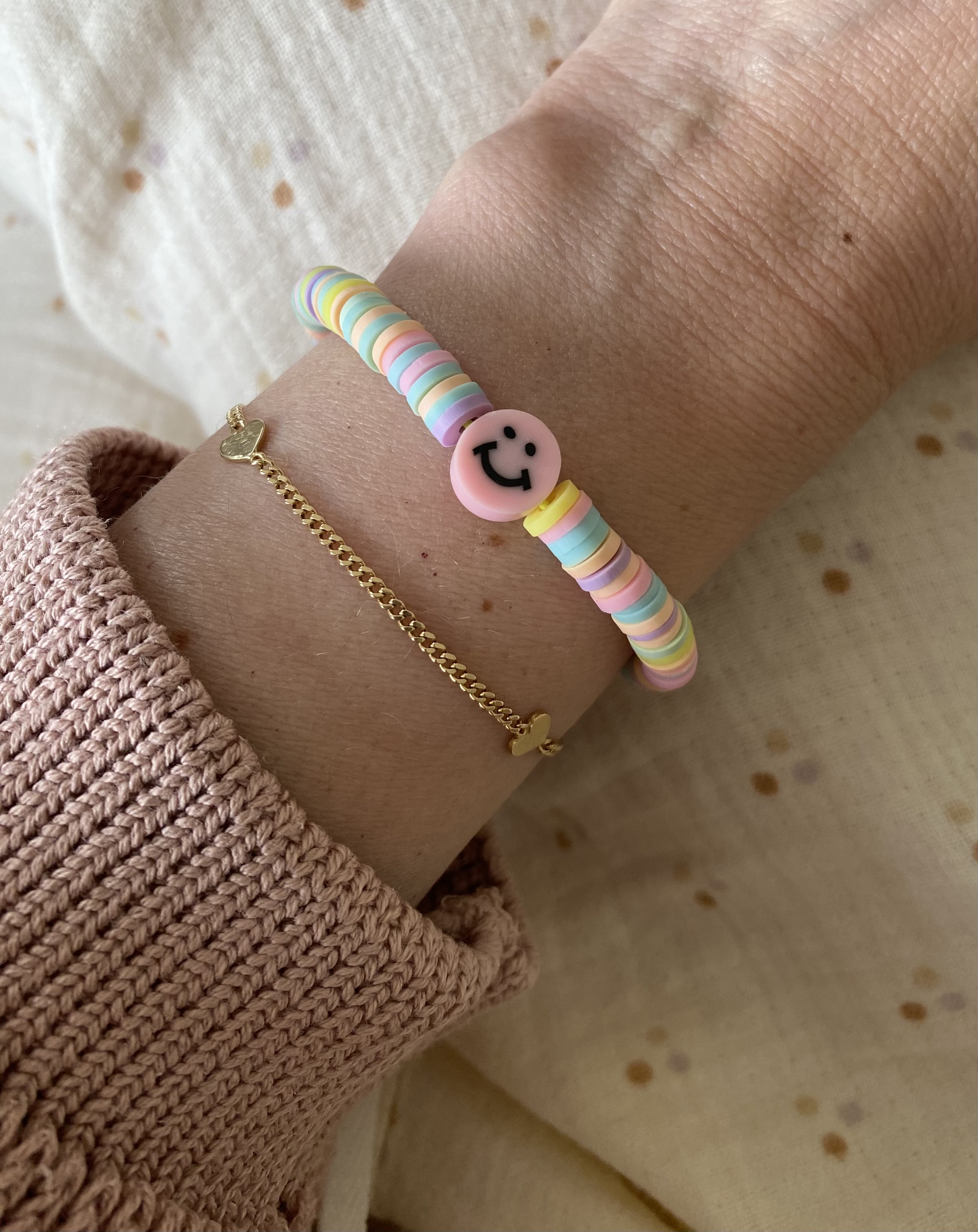 Armband, bunte Scheibenperlen, rosa Smiley-Anhänger, goldene Kette mit Herz, gestrickter Ärmel in Altrosa.