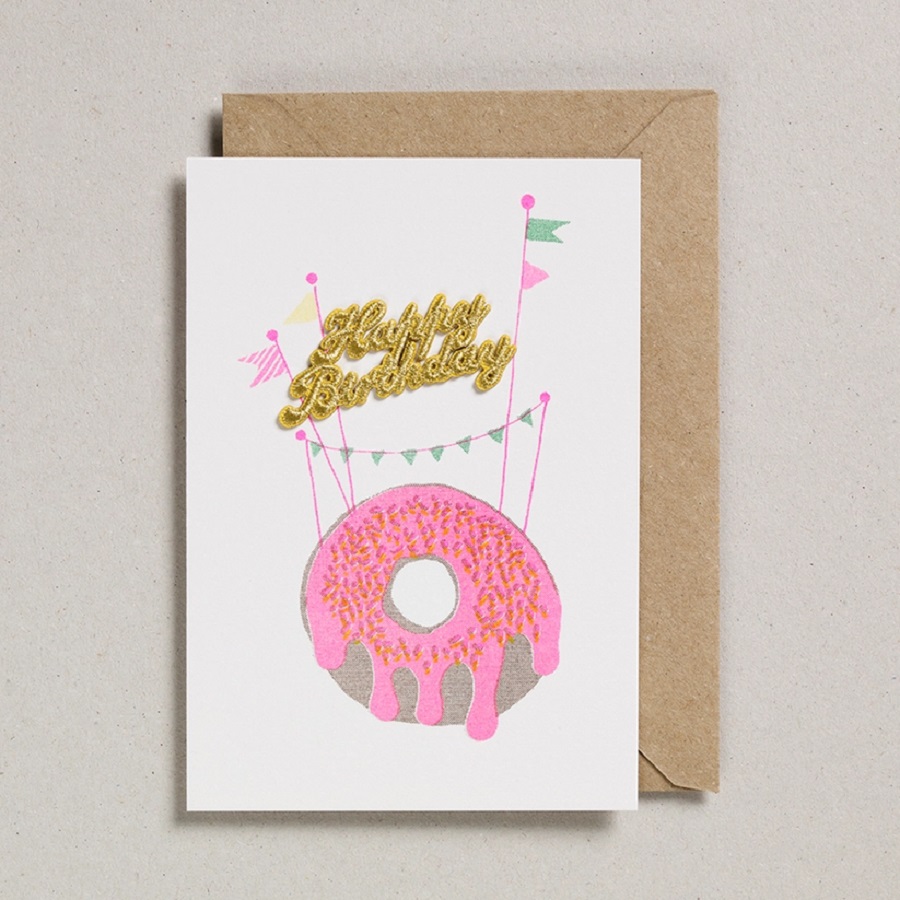 8d2d3349692f8e53d24fe0c02bb511e002a3a2c28a2ad02b7060478d4d054357 Grußkarte, weiß, Motiv: Donut mit pinkem Zuckerguss, goldener Geburtstags-Schriftzug, bunte Wimpel, brauner Umschlag.