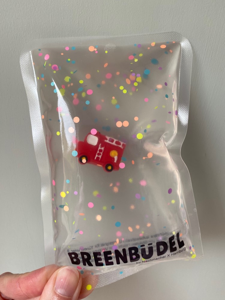 Transparente Verpackung, Konfettimuster, rotes Feuerwehrauto, Aufdruck "BREENBÜDEL", handgehalten.