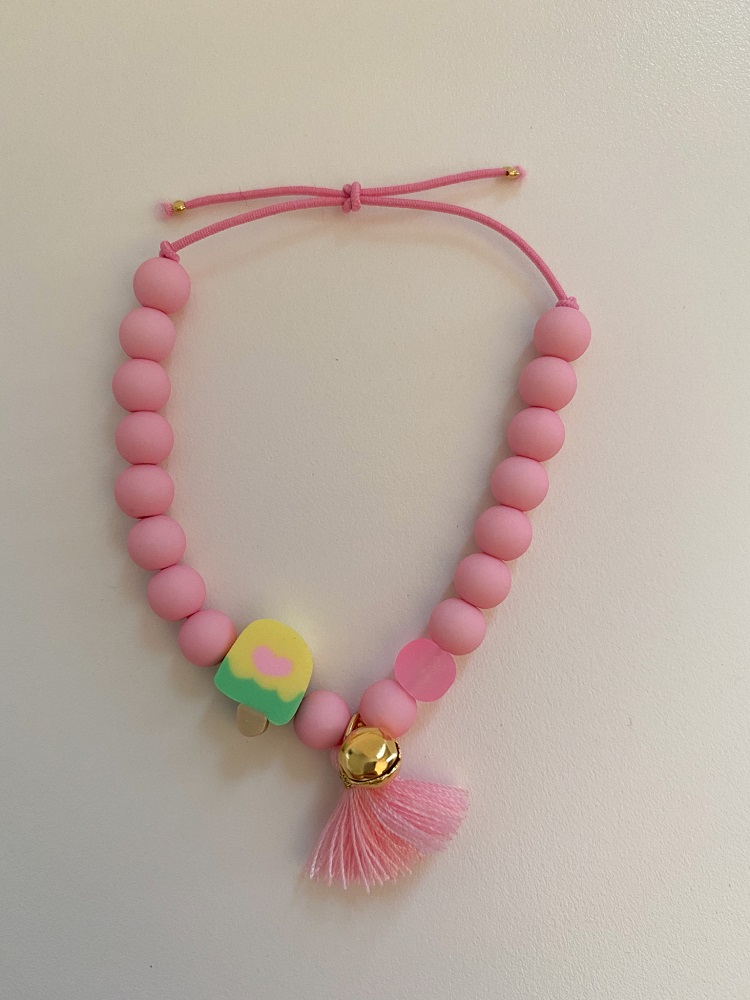 IMG_5228 Rosa Halskette mit runden Perlen, verstellbarer Schnur, gelb-grünem Anhänger mit Herzmotiv, goldener Glocke und rosa Quaste.