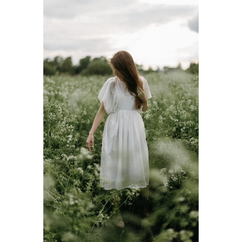 405439_large_yiEAGjepGT1LFO29ElJR Person mit langem Haar, weißes Kleid, Kurzarm, Blumenmotiv, grüne Wiese im Hintergrund.