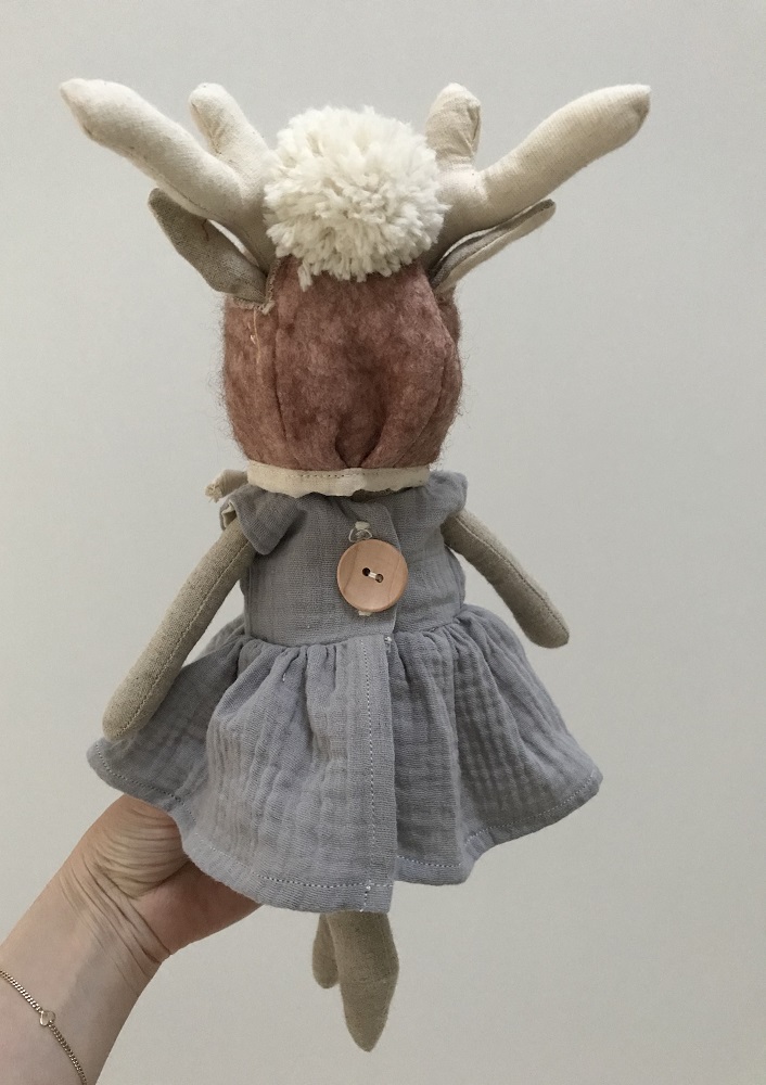 IMG_0629-002 Stofftier Hirsch, Filz, braun, cremefarbene Geweih-Ohren, flauschiges Pom-Pom-Haar, hellgraues Baumwollkleid, großer Holzknopf, von Hand gehalten.
