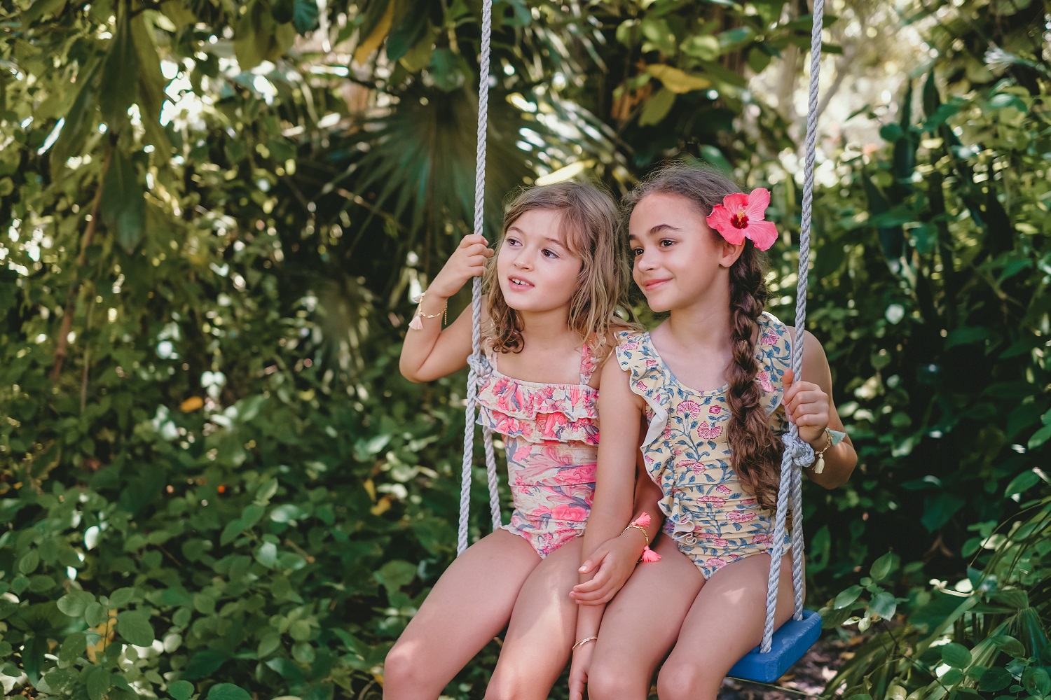girls-bathing-suit-zacatecas-pink-flowers-4 Kinderbademode, zwei Mädchen, bunte Badeanzüge mit Rüschen, Blumenmuster, rosa und blau, Schaukel, tropische Umgebung