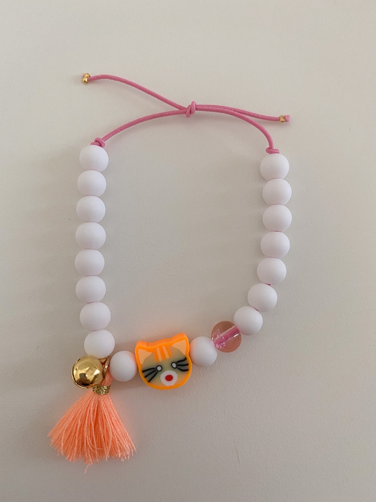 IMG_5316 Armband, weiße Perlen, orangefarbene Quaste, goldene Glocke, Katzenanhänger, pinkes Band.