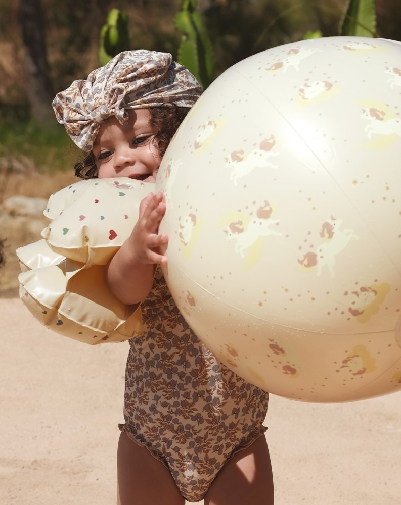 KS4868-BEACH-BALL-UNICORN-Extra-1 Baby mit Schwimmflügeln, geblümter Badeanzug, passendes Kopftuch, hellgelber Strandball mit Einhornaufdruck.