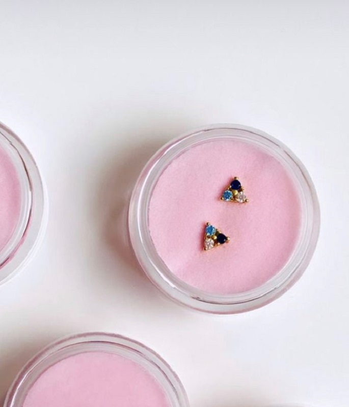 IMG_0588_2 Runde Schmuckdose, rosa Innenpolster, enthaltener Ohrstecker in Dreieckform, goldfarben, blaue und weiße Steine, transparenter Deckel.